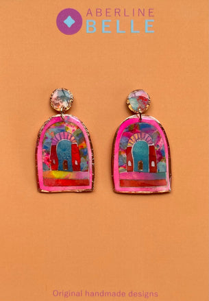 A pair of colorful handmade earrings displayed on a peach-colored backing card. The earrings feature a vibrant, multicolored arch design with pink borders and gold-toned metal settings.