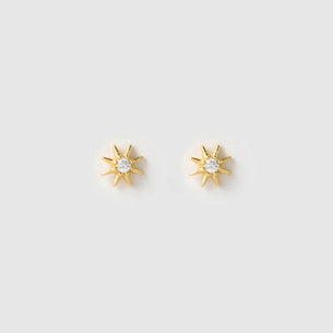 A pair of gold starburst stud earrings with clear round-cut gemstones in the center, displayed on a light gray background.